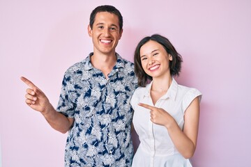 Beautiful couple wearing casual clothes smiling and looking at the camera pointing with two hands and fingers to the side.