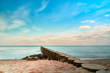 Sandy beach by the sea, wooden breakwater goes into the blue sky horizon