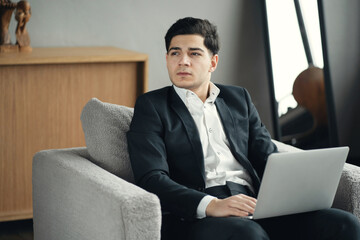 economist a man of European appearance works on a laptop computer, invests money on the stock exchange. sitting in a new stylish office sofa. favorite job manager