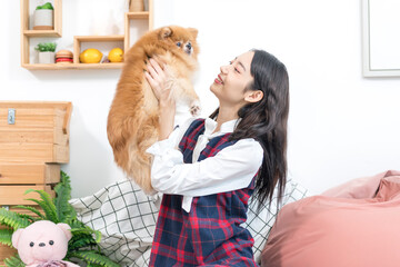 An Asian woman is holding a Pomeranian dog in the living room. 