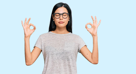 Fototapeta na wymiar Beautiful young woman wearing casual clothes and glasses relax and smiling with eyes closed doing meditation gesture with fingers. yoga concept.