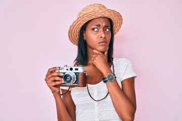 Young african american woman wearing summer hat holding vintage camera touching painful neck, sore throat for flu, clod and infection