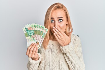 Beautiful caucasian woman holding hong kong 50 dollars banknotes covering mouth with hand, shocked and afraid for mistake. surprised expression