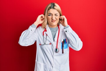 Young caucasian woman wearing doctor uniform and stethoscope covering ears with fingers with...