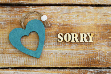 Sorry written with wooden letters on rustic surface and wooden heart
