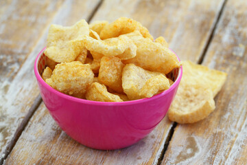 Crispy pork cracklings in pink bowl on rustic wooden surface

