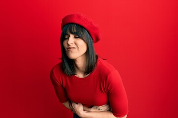 Naklejka premium Young hispanic woman wearing french look with beret with hand on stomach because nausea, painful disease feeling unwell. ache concept.
