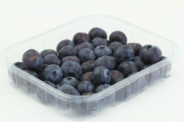 Fresh sweet blueberries in transparent plastic box on white background
