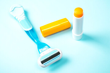 Women razor and lip gloss isolated on a blue background. Close-up. Beauty concept.