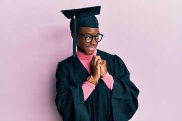 Young african american girl wearing graduation cap and ceremony robe laughing nervous and excited...
