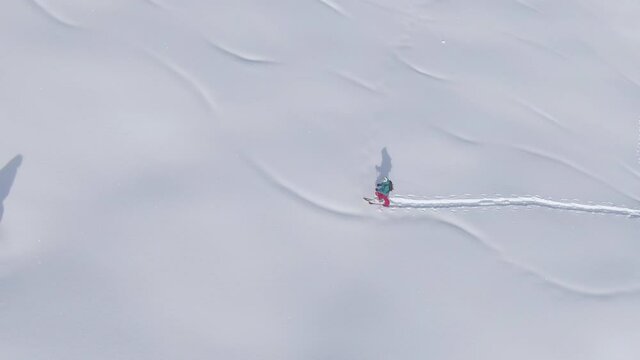 DRONE: Scenic drone shot of wintry landscape surrounding a female ski tourer powder chasing in the Julian Alps. Fit woman on active vacation hikes up a snowy meadow during a fun splitboarding trip.
