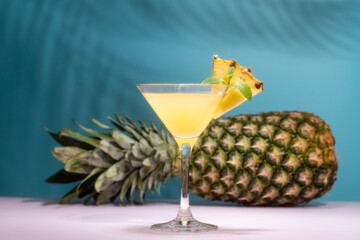 Refreshing pineapple cocktail with slice of pineapple and mint in front of shadow of palm leaves in a shining sun.