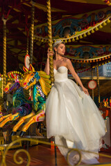bride in white wedding dress sits on carousel horses,