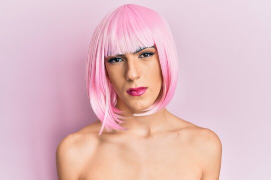Young man wearing woman make up wearing pink wig relaxed with serious expression on face. simple and natural looking at the camera.