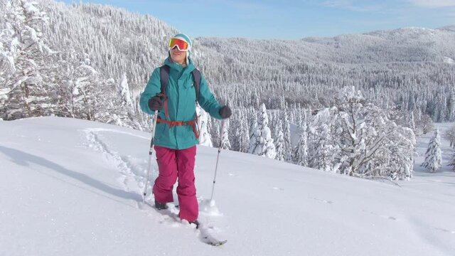 CLOSE UP: Active female tourist ski touring in the gorgeous Julian Alps hikes up a snowy hill. Young Caucasian woman on splitboarding trip treks across a snow covered meadow on a sunny winter day.