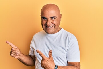 Mature middle east man wearing casual white tshirt smiling and looking at the camera pointing with two hands and fingers to the side.