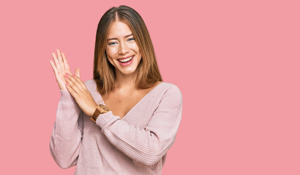 Beautiful blonde woman wearing casual winter pink sweater clapping and applauding happy and joyful, smiling proud hands together