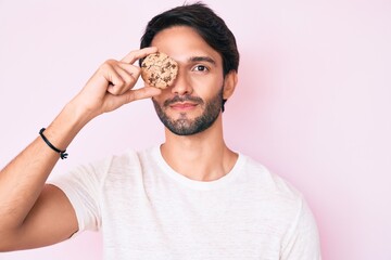 Handsome hispanic man holding cookie thinking attitude and sober expression looking self confident