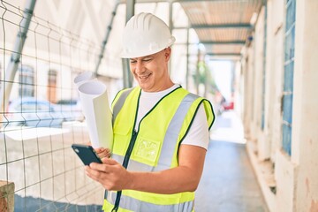 Middle age architect man using smartphone and holding blueprints at the city.