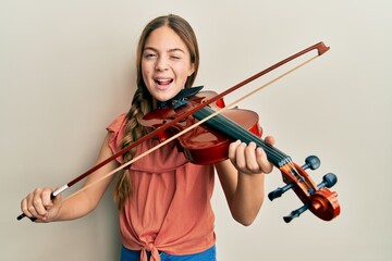 Beautiful brunette little girl playing violin winking looking at the camera with sexy expression,...