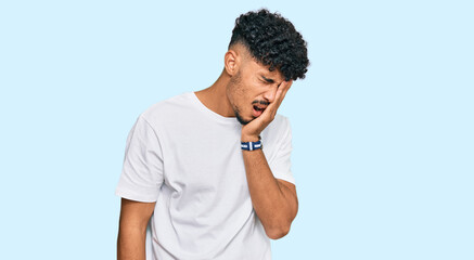 Young arab man wearing casual white t shirt yawning tired covering half face, eye and mouth with hand. face hurts in pain.