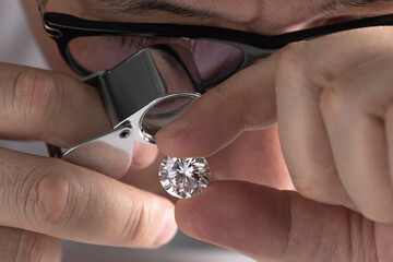 Jeweller asian man looking at diamond through magnifying glass. Diamond dealer evaluating and...