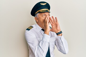 Handsome middle age mature man wearing airplane pilot uniform shouting angry out loud with hands over mouth © Krakenimages.com