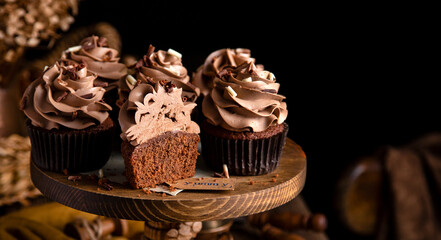 homemade tasty chocolate cupcakes with chocolate cream on wooden cake stand on rustic table. selective focus