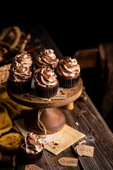 homemade tasty chocolate cupcakes with chocolate cream on wooden cake stand on rustic table. selective focus