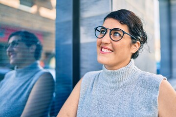 Young plus size woman smiling happy leaning on the wall at the city.