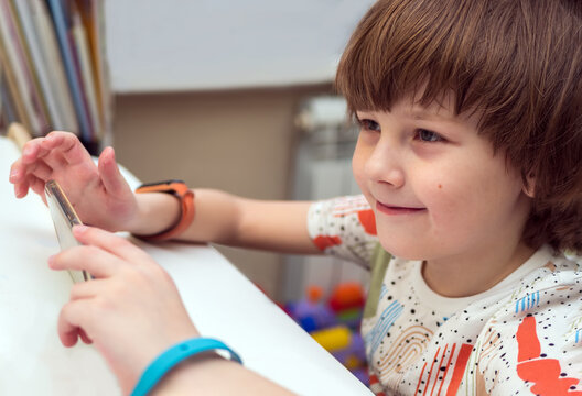 Eight years old caucasian boy in casual wear is using smartphone at home. Home education concept.