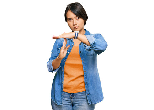 Young beautiful hispanic woman with short hair wearing casual denim jacket doing time out gesture with hands, frustrated and serious face