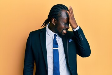 Handsome young black man wearing business suit and tie surprised with hand on head for mistake,...
