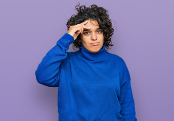 Fototapeta na wymiar Young hispanic woman with curly hair wearing turtleneck sweater worried and stressed about a problem with hand on forehead, nervous and anxious for crisis