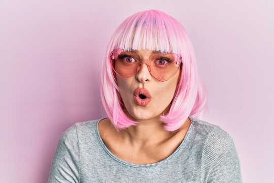 Young caucasian woman wearing pink wig and heart sunglasses scared and amazed with open mouth for surprise, disbelief face