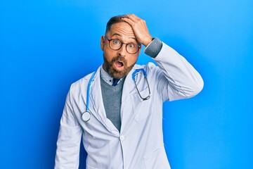 Handsome middle age man wearing doctor uniform and stethoscope surprised with hand on head for...