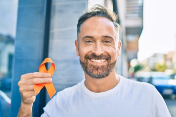 Middle age handsome man smiling happy holding orange ribbon at the city.