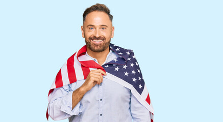 Handsome middle age man holding united states flag looking positive and happy standing and smiling with a confident smile showing teeth