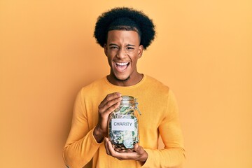 African american man with afro hair holding charity jar with money smiling and laughing hard out...