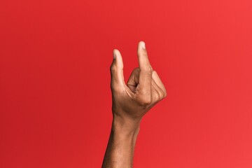 Hand of hispanic man over red isolated background picking and taking invisible thing, holding object with fingers showing space