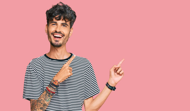 Young hispanic man wearing casual clothes smiling and looking at the camera pointing with two hands and fingers to the side.