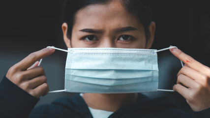 Young Asian woman holding face mask and looking to camera feeling serious.