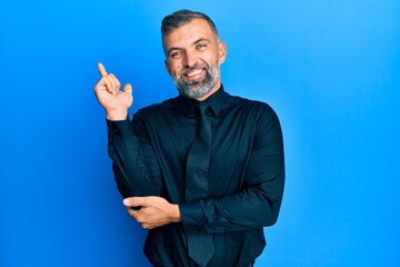 Middle age handsome man wearing business shirt and tie with a big smile on face, pointing with hand and finger to the side looking at the camera.