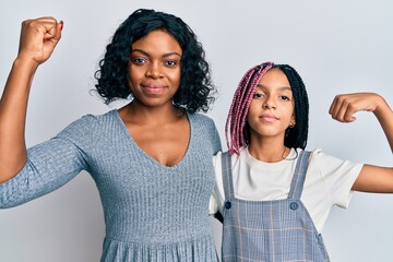 Beautiful african american mother and daughter wearing casual clothes and hugging strong person showing arm muscle, confident and proud of power