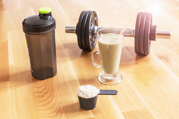 Scoop of protein powder, sports drink in glass, shaker and heavy black dumbell.