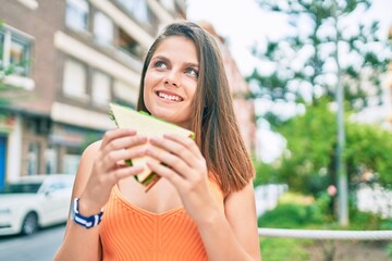 Young middle east girl smiling happy eating sandwich at the city.