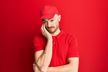 Young redhead man wearing delivery uniform and cap thinking looking tired and bored with depression problems with crossed arms.