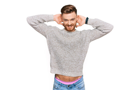 Young redhead man wearing casual winter sweater relaxing and stretching, arms and hands behind head and neck smiling happy