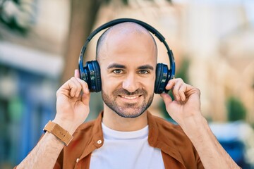 Young hispanic bald man smiling happy using headphones at the city