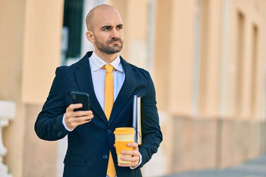 Young hispanic bald businessman with serious expression using smartphone drinking coffee at the city.